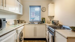 A compact kitchen with a washing machine, microwave, sink, and stove. - Sandringham Court Flat 4 (Swanage)