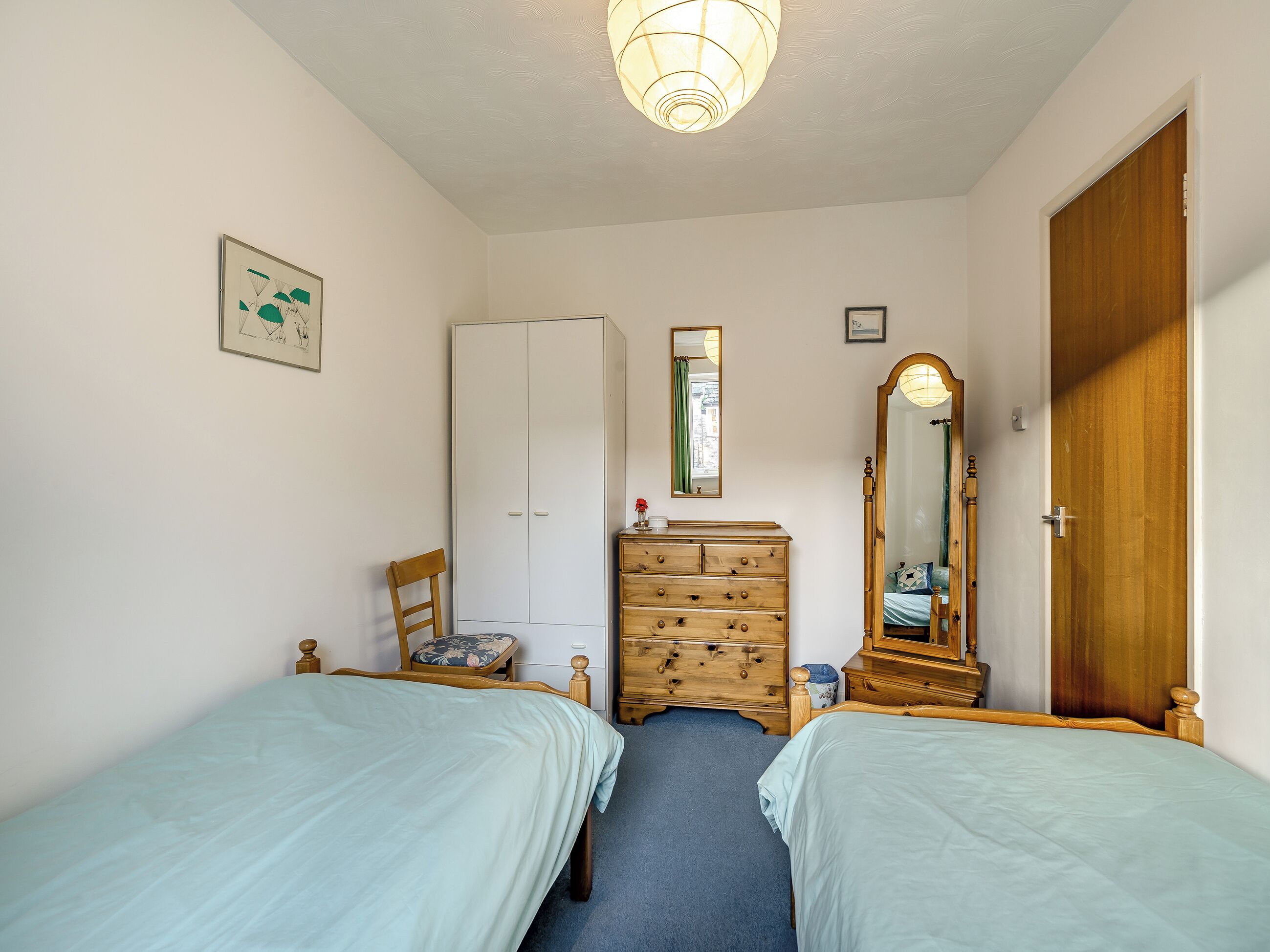 Une chambre avec deux lits, une armoire, une commode, un miroir et un luminaire au plafond.