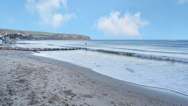 A beach with a wooden jetty, a clear sky, and a distant coastline with buildings. - Sandringham Court Flat 4 (Swanage)