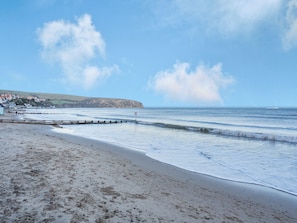 A beach with a wooden jetty, a clear sky, and a distant coastline with buildings. - Sandringham Court Flat 4 (Swanage)