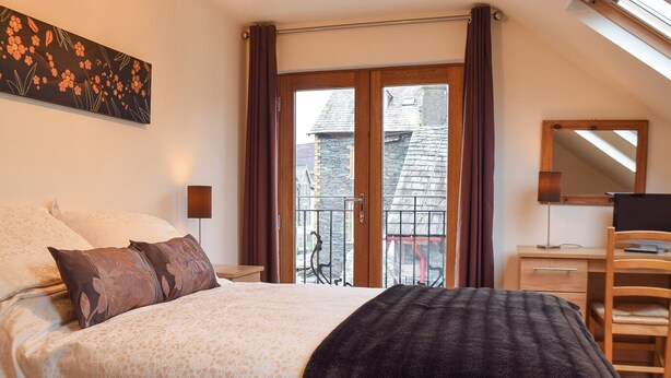 Un dormitorio con cama, escritorio, silla y balcón con vistas a edificios.