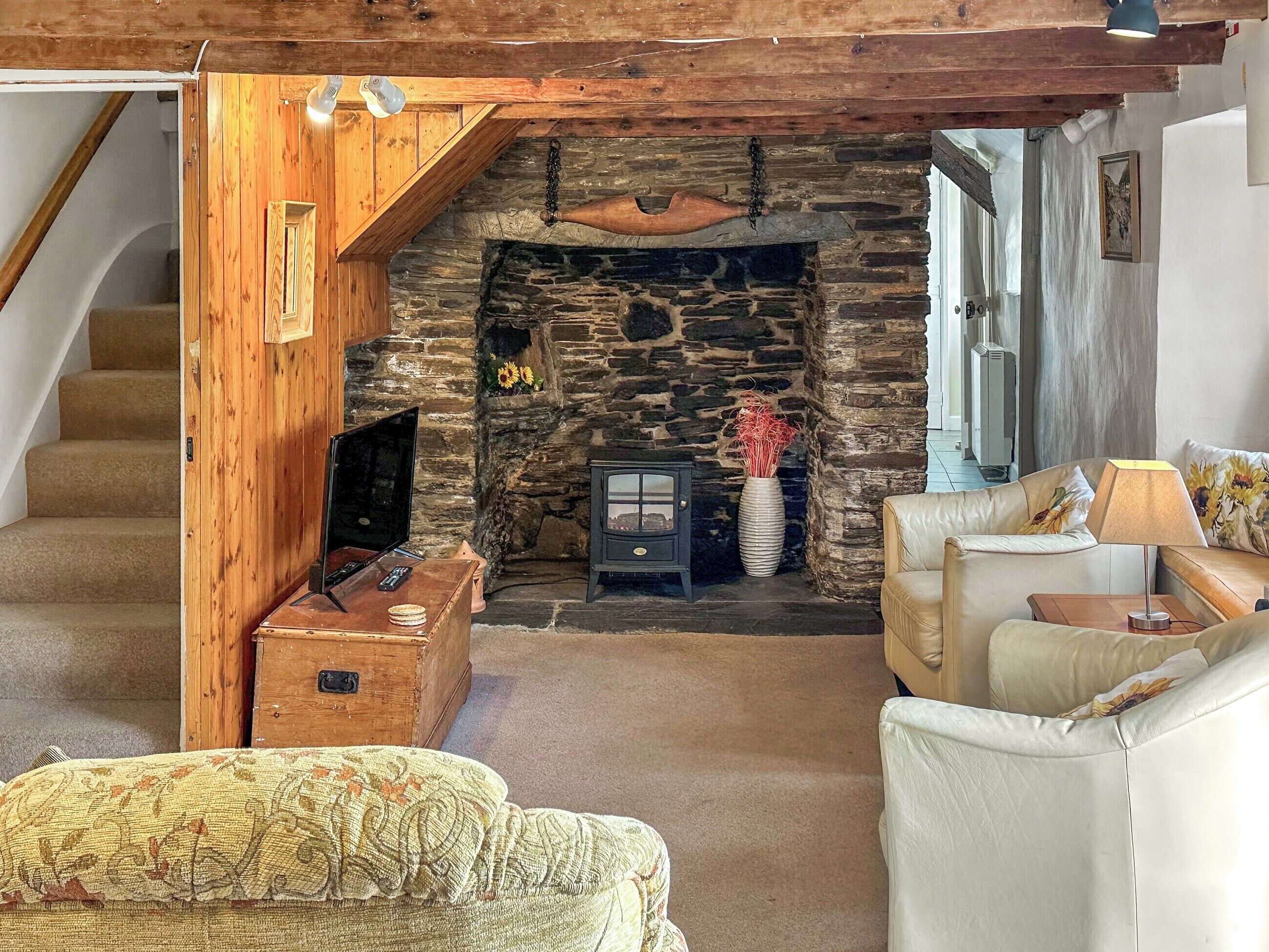 Uma sala de estar aconchegante com lareira de pedra, vigas de madeira, televisão e um sofá.