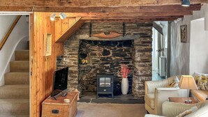 Uma sala de estar aconchegante com lareira de pedra, vigas de madeira, televisão e um sofá.