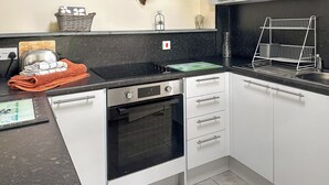 Uma cozinha moderna com armários brancos, bancada preta e forno embutido.