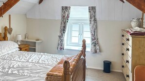 Quarto com cama de madeira, mesa de cabeceira, cômoda e janela com cortinas florais.