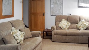 A living room with two beige sofas, each with floral cushions, a wooden door, and a small wooden table. - 1 bedroom accommodation in Thornthwaite, near Keswick (Thornthwaite, near Keswick)
