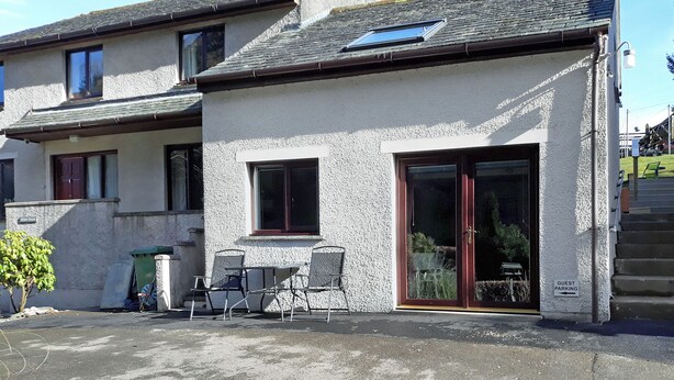 A building with a patio area, a guest parking sign, and a small table with chairs. - 1 bedroom accommodation in Thornthwaite, near Keswick (Thornthwaite, near Keswick)