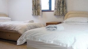 A hotel room with two beds, a wooden nightstand, and a window with floral curtains. - 1 bedroom accommodation in Thornthwaite, near Keswick (Thornthwaite, near Keswick)