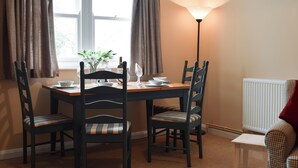 Un coin repas avec une table dressée pour quatre personnes, deux chaises de chaque côté, une lampe et une fenêtre avec des rideaux.