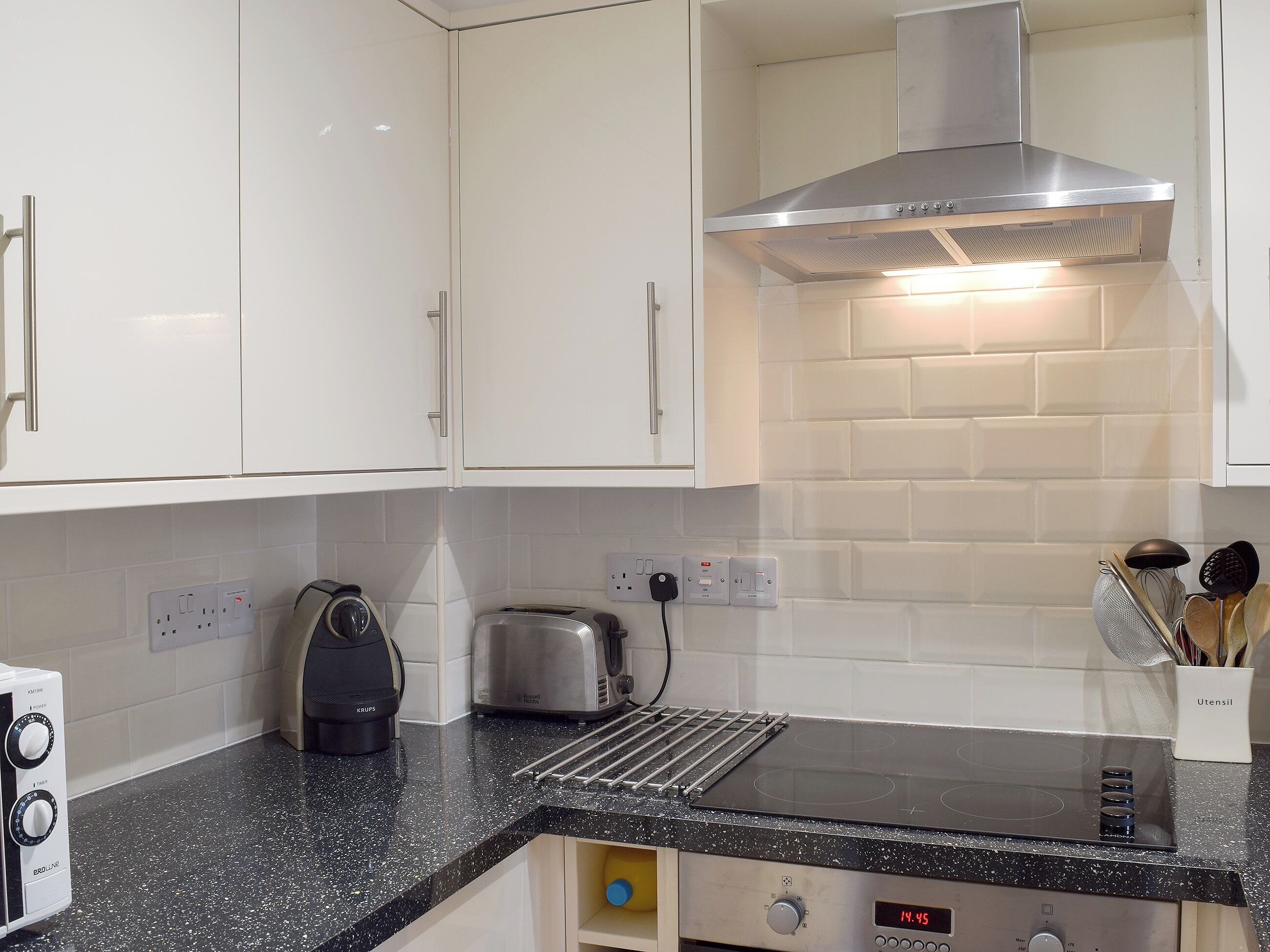 A kitchen with white cabinets, a black countertop, a stainless steel range hood, a toaster, and a kettle.