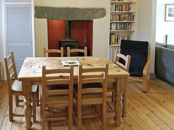 A dining area with a wooden table and chairs, a bookshelf, and a fireplace.