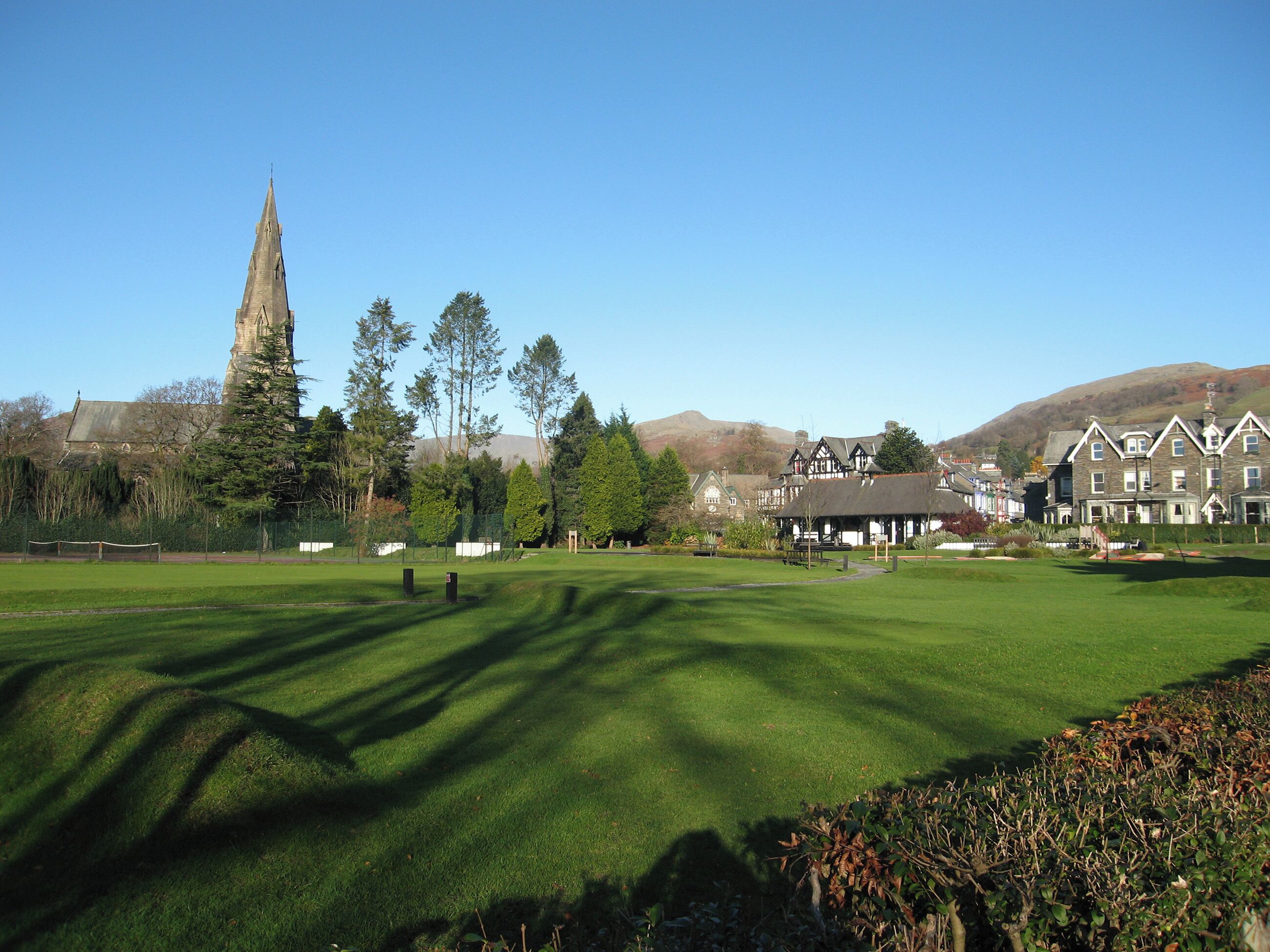 A golf course with a church spire, residential buildings, and a mountain in the background.