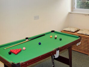 A pool table with balls, a cue stick, and a wooden side table with cushions.