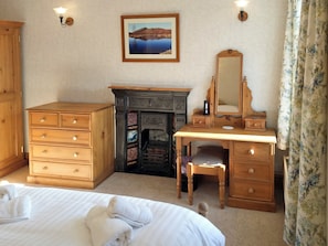 A bedroom with a wooden dresser, a desk with a mirror, a fireplace, and a bed with towels.