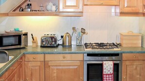 A kitchen with wooden cabinets, a microwave, a toaster, a kettle, and a gas stove. - 2 bedroom accommodation in Ambleside (Ambleside)