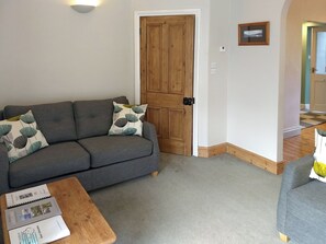 A living room with a grey sofa, a wooden door, and a small table with magazines. - 2 bedroom accommodation in Ambleside (Ambleside)