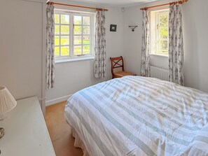 Un dormitorio con cama, una silla, una ventana con cortinas y un radiador.