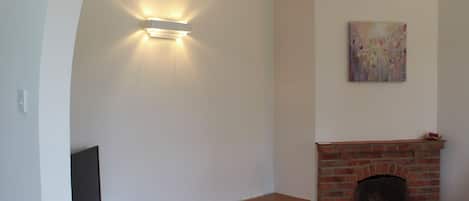 Un salon comprenant un téléviseur, une petite table en bois, une cheminée en briques et un luminaire fixé au mur.