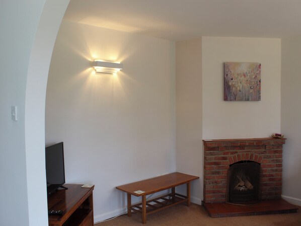 Een woonkamer met een televisie, een klein houten tafeltje, een metselwerk schoorsteen en een wandlamp.