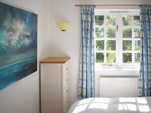 Een slaapkamer met een bed, nachtkastje, wandlamp, raam met gordijnen en een schilderij aan de muur.