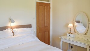 Un llit ben fet amb llençols blancs, una làmpada de nit, un mirall i una porta de fusta en una habitació amb parets color crema.