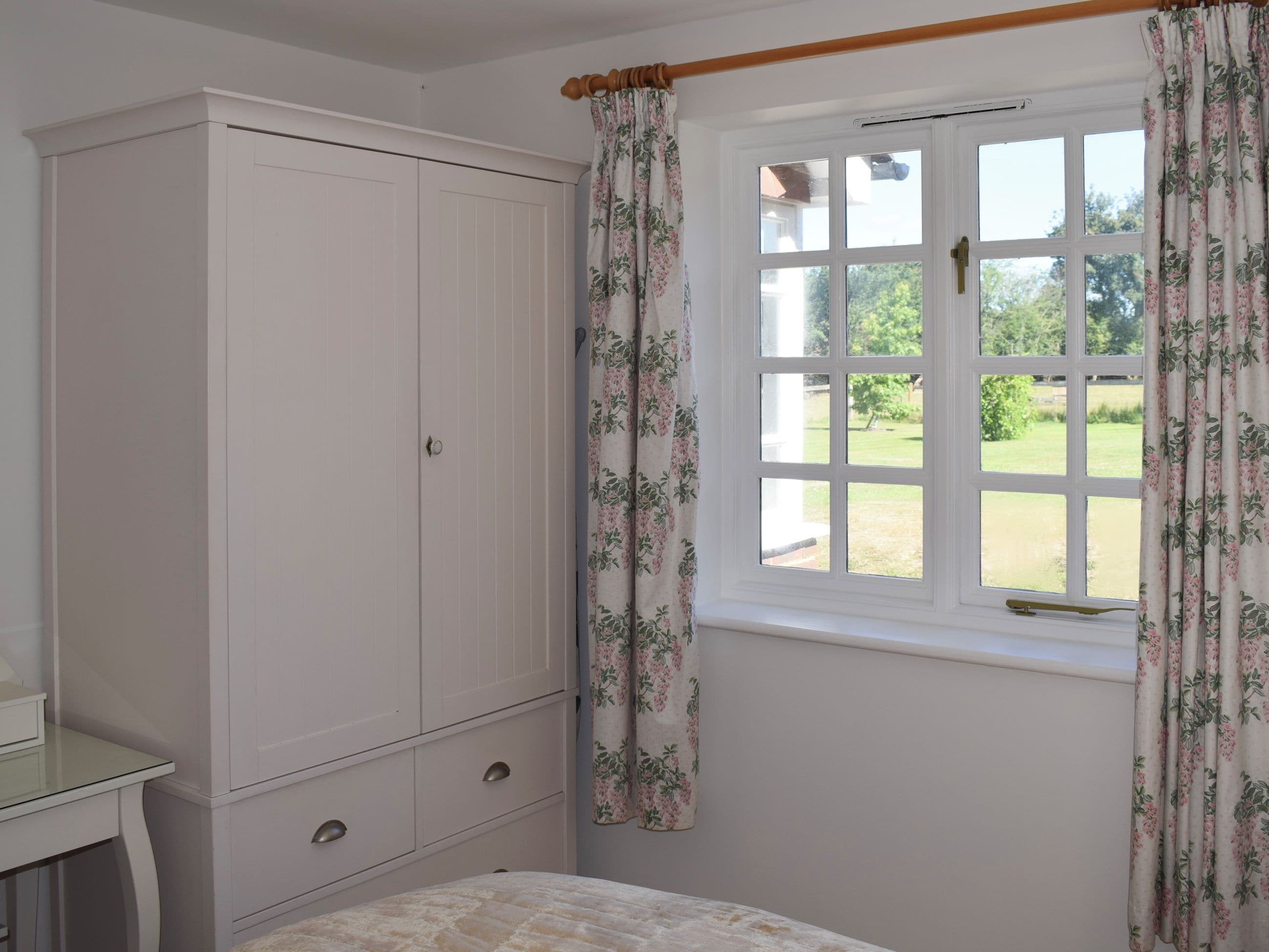 Un dormitorio con cama, armario, ventana con cortinas y vistas a un jardín.