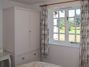 Een slaapkamer met een bed, een kledingkast, een raam met gordijnen en uitzicht op een tuin.