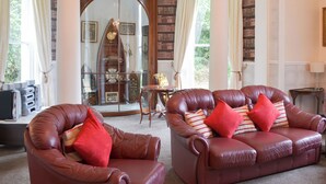 A room with leather armchairs, a wooden cabinet, and a large arched doorway leading to a library. - 2 bedroom accommodation in Liskeard (Liskeard)