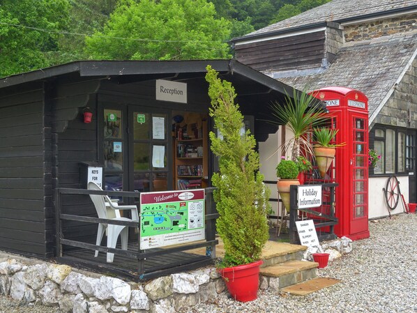 Un espace d’accueil avec un panneau indicateur, une cabine téléphonique rouge et un petit bâtiment à l’extérieur en bois.