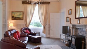 A living room with leather sofas, a fireplace, a television, and a chandelier. - 2 bedroom accommodation in Liskeard (Liskeard)