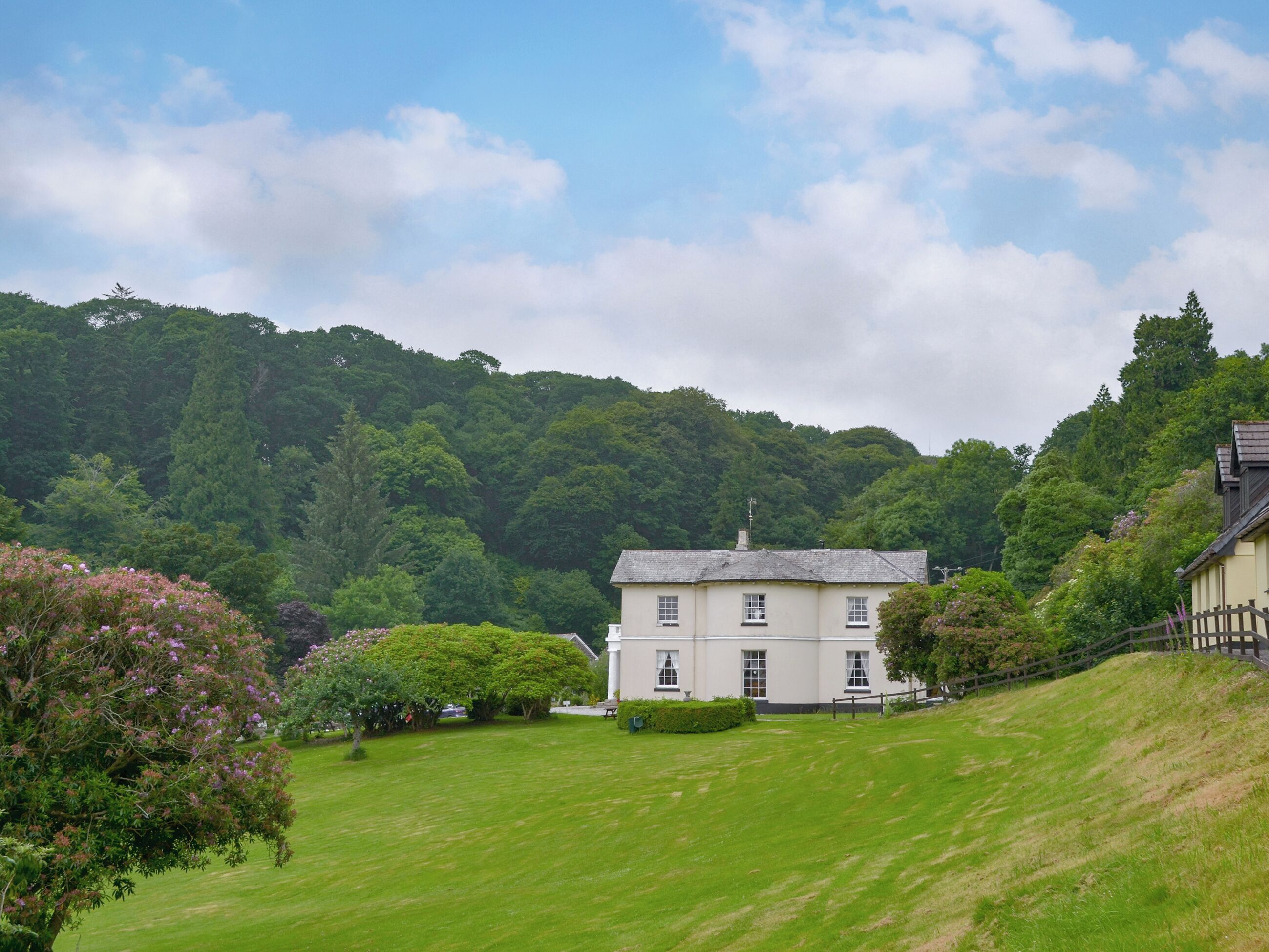 A large, single-story building with a symmetrical facade, surrounded by a well-maintained lawn and dense forested hills in the background.