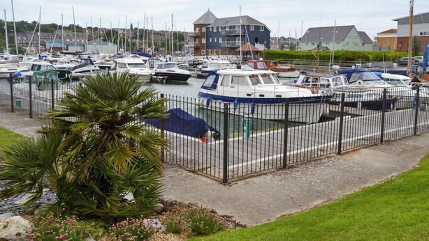 A marina with multiple boats docked, a fenced area, and a building in the background. - 3 bedroom accommodation in East Cowes (East Cowes)