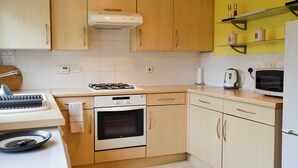 A compact kitchen with wooden cabinets, a gas stove, an oven, a microwave, and a kettle. - 3 bedroom accommodation in East Cowes (East Cowes)