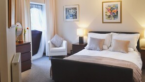 Een hotelkamer met een groot bed, een stoel, een nachtkastje, een spiegel en twee ingelijste foto's aan de muur.