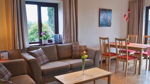 Een woonkamer met een bank, een bijzettafeltje en een eethoek met stoelen en een tafel.