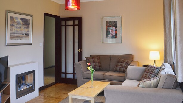Een woonkamer met een open haard, een bank, een salontafel en twee rode hanglampen.