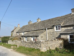 Ein Steinhhaus mit einem Strohdach, einer Steinmauer und einer schmalen Straße davor.