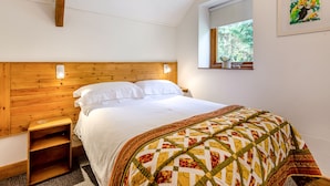 A bedroom with a wooden headboard, a bed with white linens, a colorful quilt, a nightstand, a window with a view of trees, and a painting on the wall.