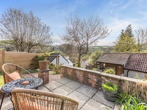 A patio with wicker furniture, a brick wall, and a view of a valley. - 1 bedroom accommodation in Berrynarbor, near Ilfracombe (Berrynarbor, near Ilfracombe)