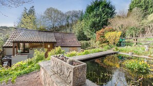 A traditional building with a tiled roof, surrounded by a garden with a pond, and a wooden fence.