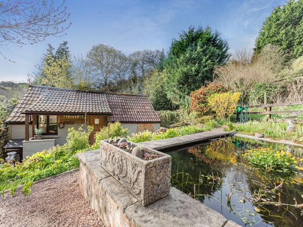 A traditional building with a tiled roof, surrounded by a garden with a pond, and a wooden fence.