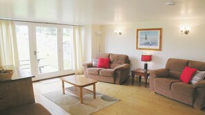 A living room with two sofas, a coffee table, and a lamp. There is a window with curtains and a door leading outside.