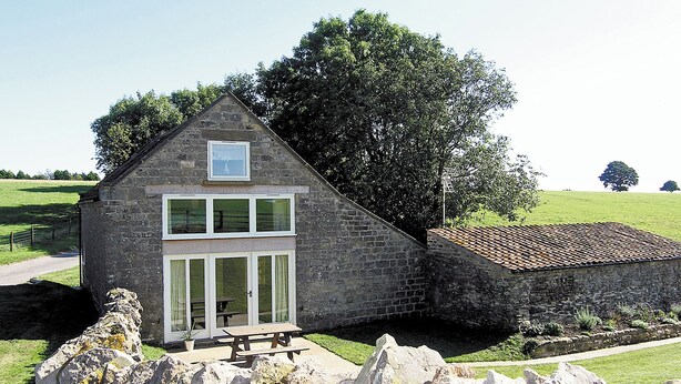 A stone building with a pitched roof, a small window, and a picnic table outside.
