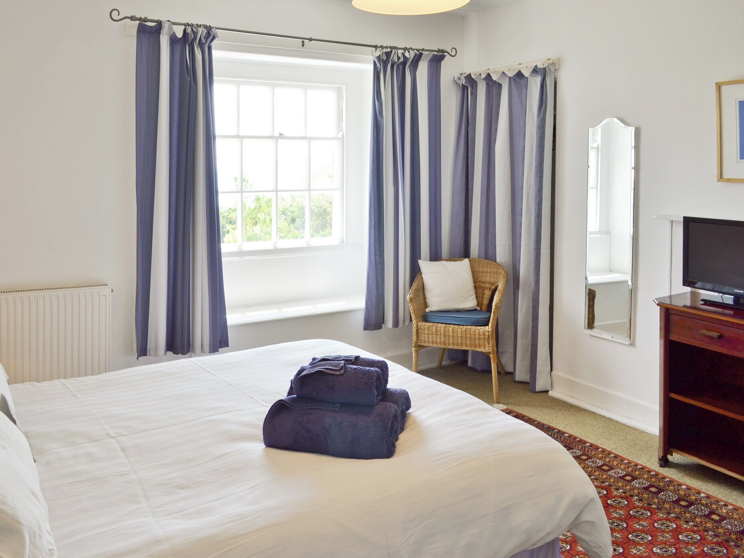 A hotel room with a large bed, a chair, a television, and a window with curtains.