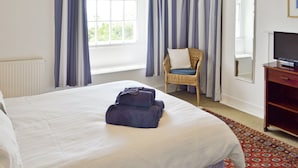 Ein Hotelzimmer mit einem großen Bett, einem Sessel, einem Fernseher und einem fenster mit Vorhängen.