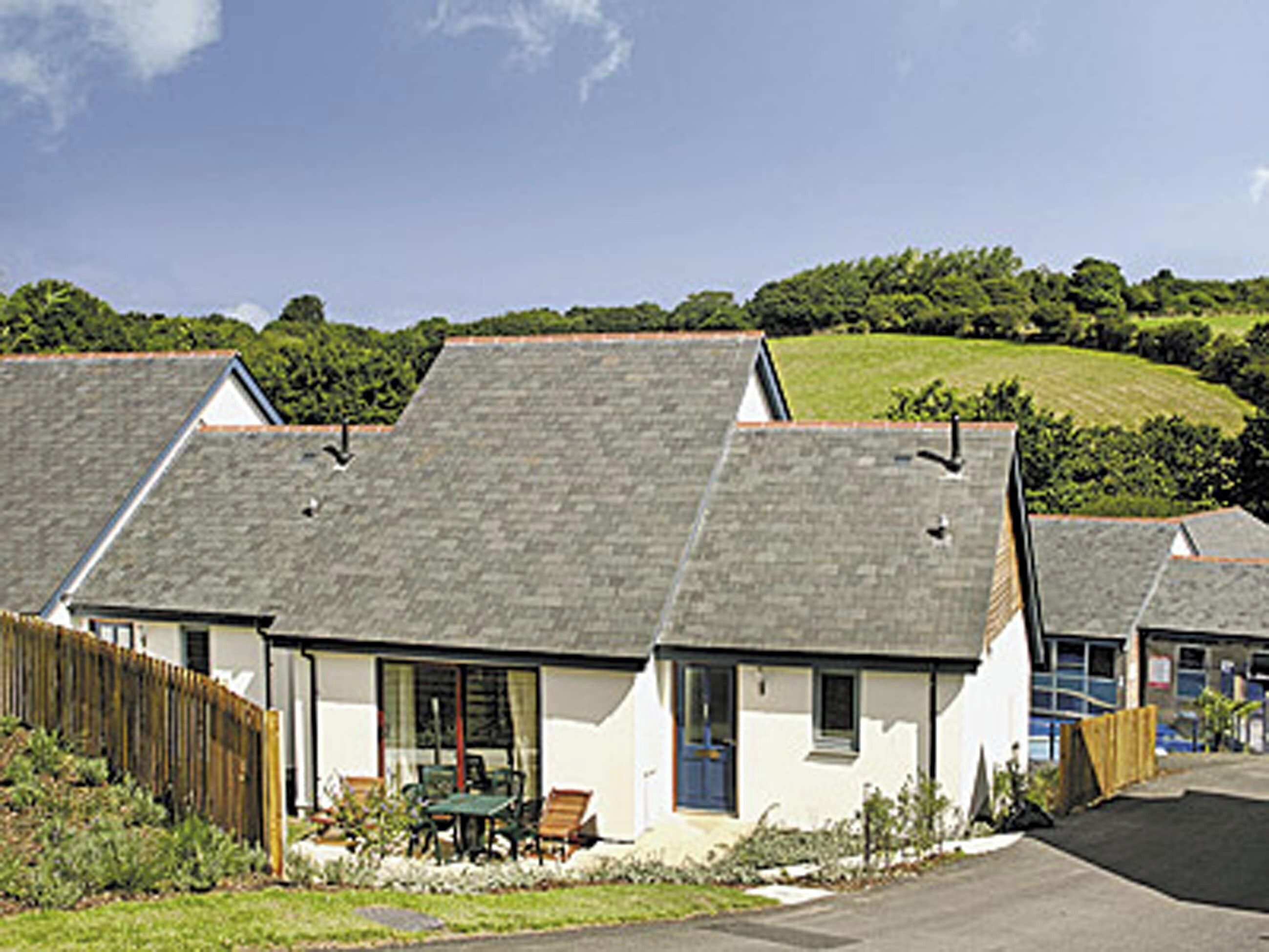 Une rangée de maisons blanches aux toits gris, une clôture en bois et, au fond, une colline verdoyante.