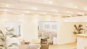 Un interior moderno con muebles blancos, incluidas mesas y sillas redondas, y una zona de bar.