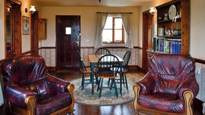 A room with a wooden dining table, two leather armchairs, a chandelier, a bookshelf, and a door. - 1 bedroom accommodation in Evershot (Evershot)