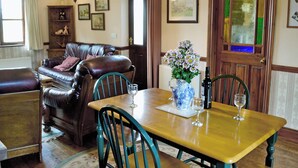 A dining area with a wooden table, chairs, a vase with flowers, and a bottle of wine. - 1 bedroom accommodation in Evershot (Evershot)
