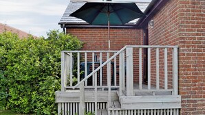 A wooden deck with a metal railing, a brick wall, and a green umbrella. - 1 bedroom accommodation in Evershot (Evershot)